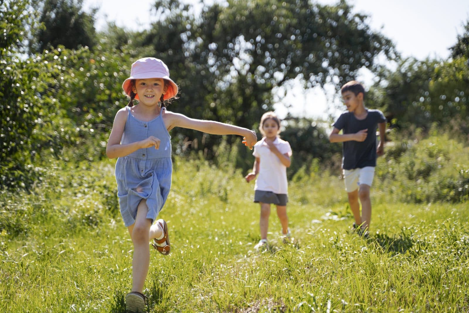 Three children running and playing in a sunlit grass field